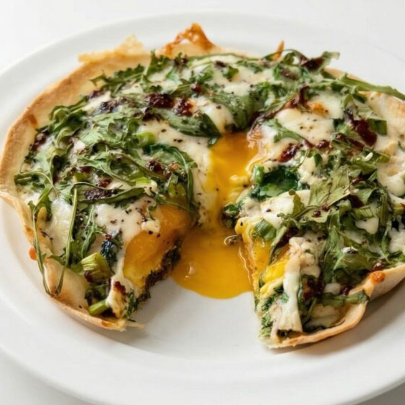 Low FODMAP crispy tortilla egg bake with spinach, feta, and arugula served on a white plate with a runny yolk