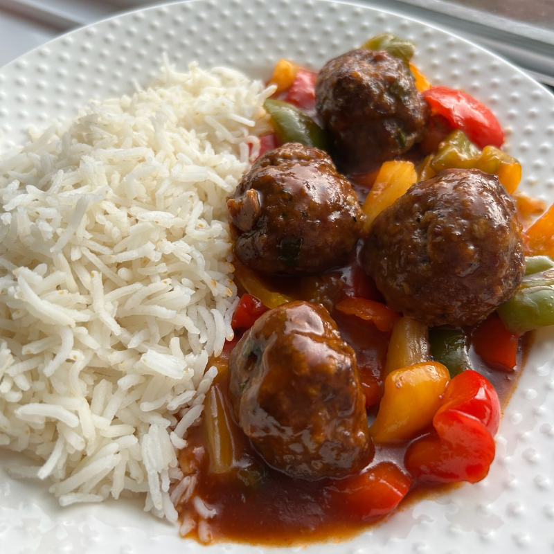 Low FODMAP sweet and sour meatballs with colorful bell peppers in glossy sauce served over white rice on a white plate