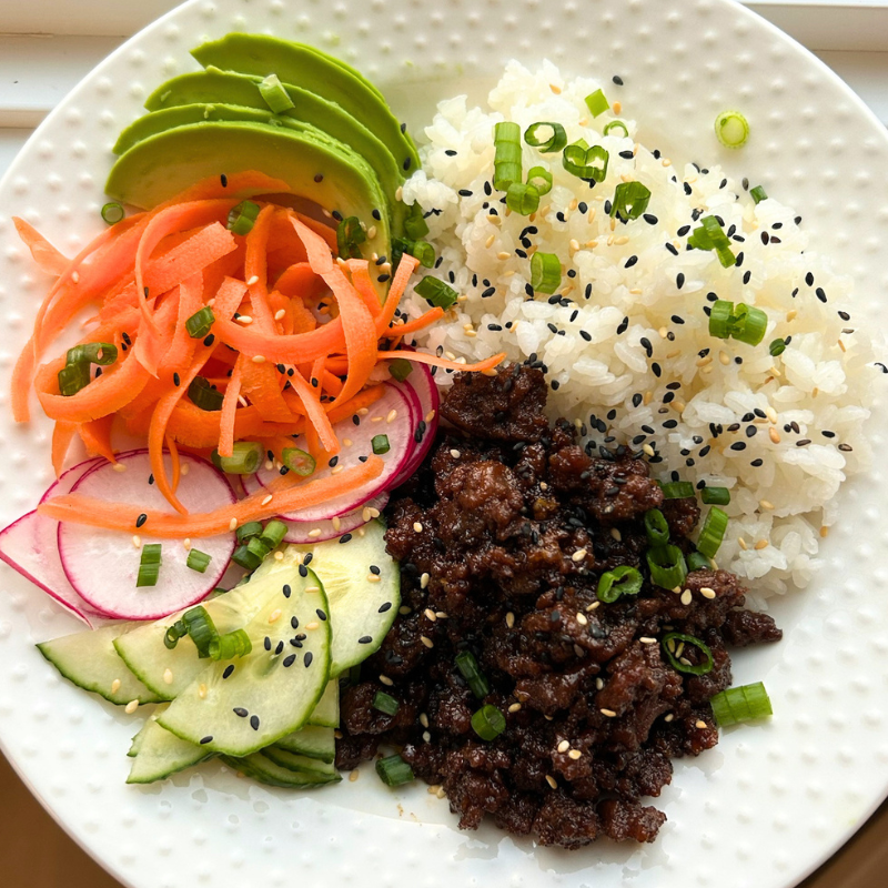 Low FODMAP Korean ground beef bowl with seasoned beef, avocado, carrots, radishes, cucumber, and sesame seeds over white rice