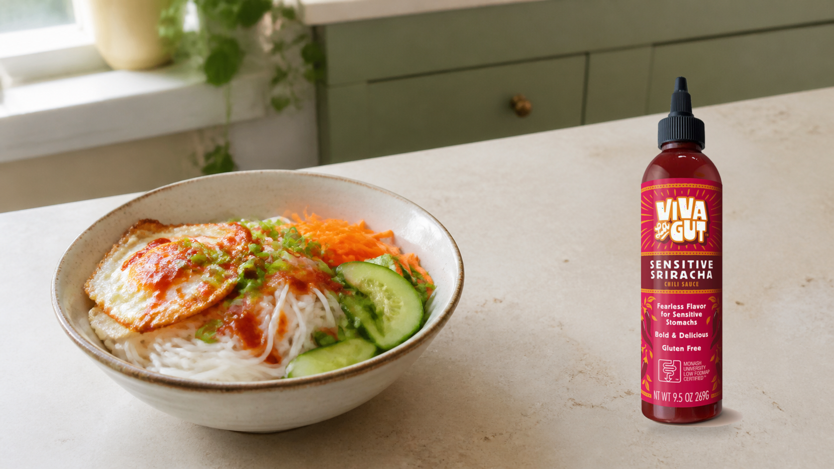 Viva La Gut Monash Certified Low FODMAP Sensitive Sriracha beside a rice noodle bowl with fried egg, chili sauce, cooked shredded carrots, cucumber, and green onion tops