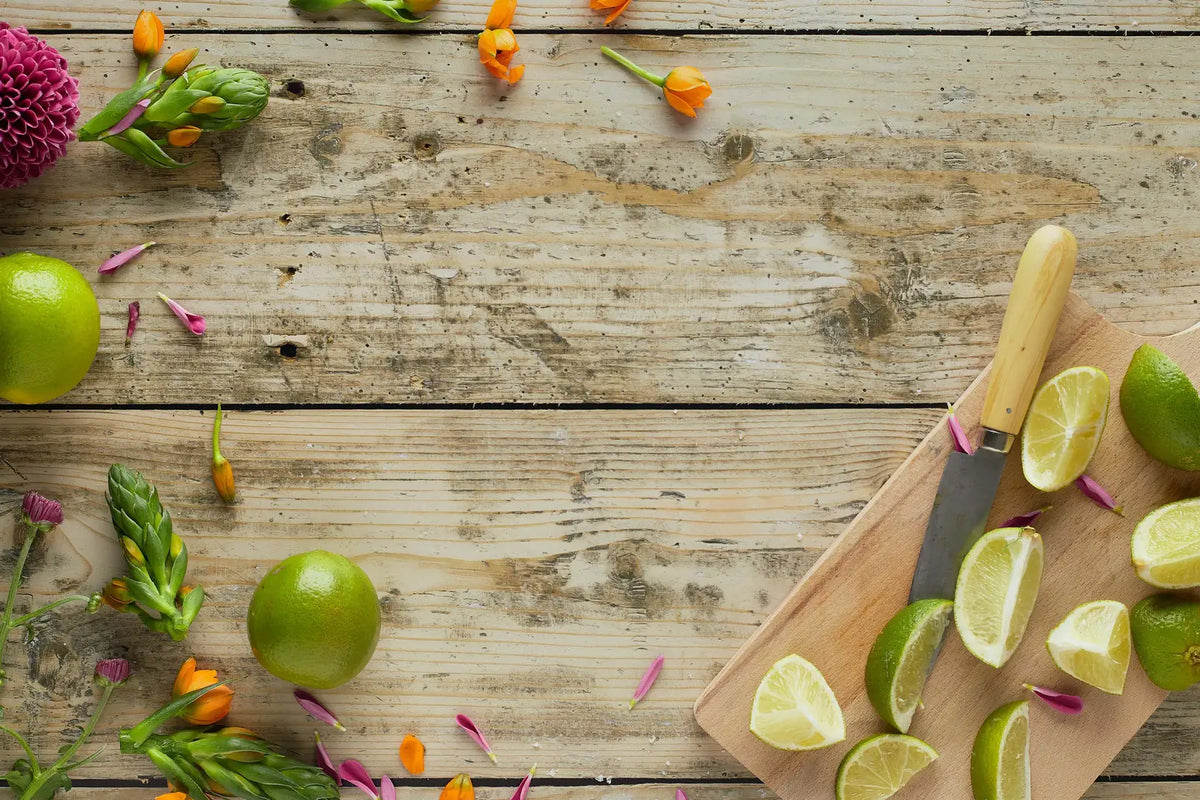 Fresh limes, flowers, and a kitchen knife on a rustic wooden table